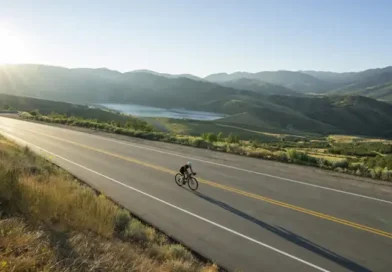 Ciclista solitario practica cicloturismo en California en una ruta bordeando un reservorio de agua durante la Golden Hour, montando una bicicleta gravel Specialized con alforjas Ortlieb. Esta imagen captura la esencia del 'Golden State' y es perfecta para acompañar artículos sobre rutas de aventura y seguros de viaje específicos para EE. UU.