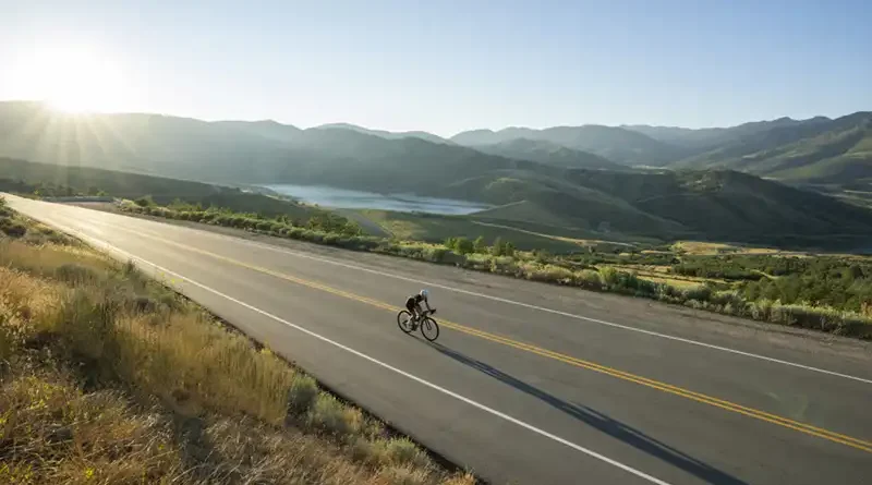 Ciclista solitario practica cicloturismo en California en una ruta bordeando un reservorio de agua durante la Golden Hour, montando una bicicleta gravel Specialized con alforjas Ortlieb. Esta imagen captura la esencia del 'Golden State' y es perfecta para acompañar artículos sobre rutas de aventura y seguros de viaje específicos para EE. UU.